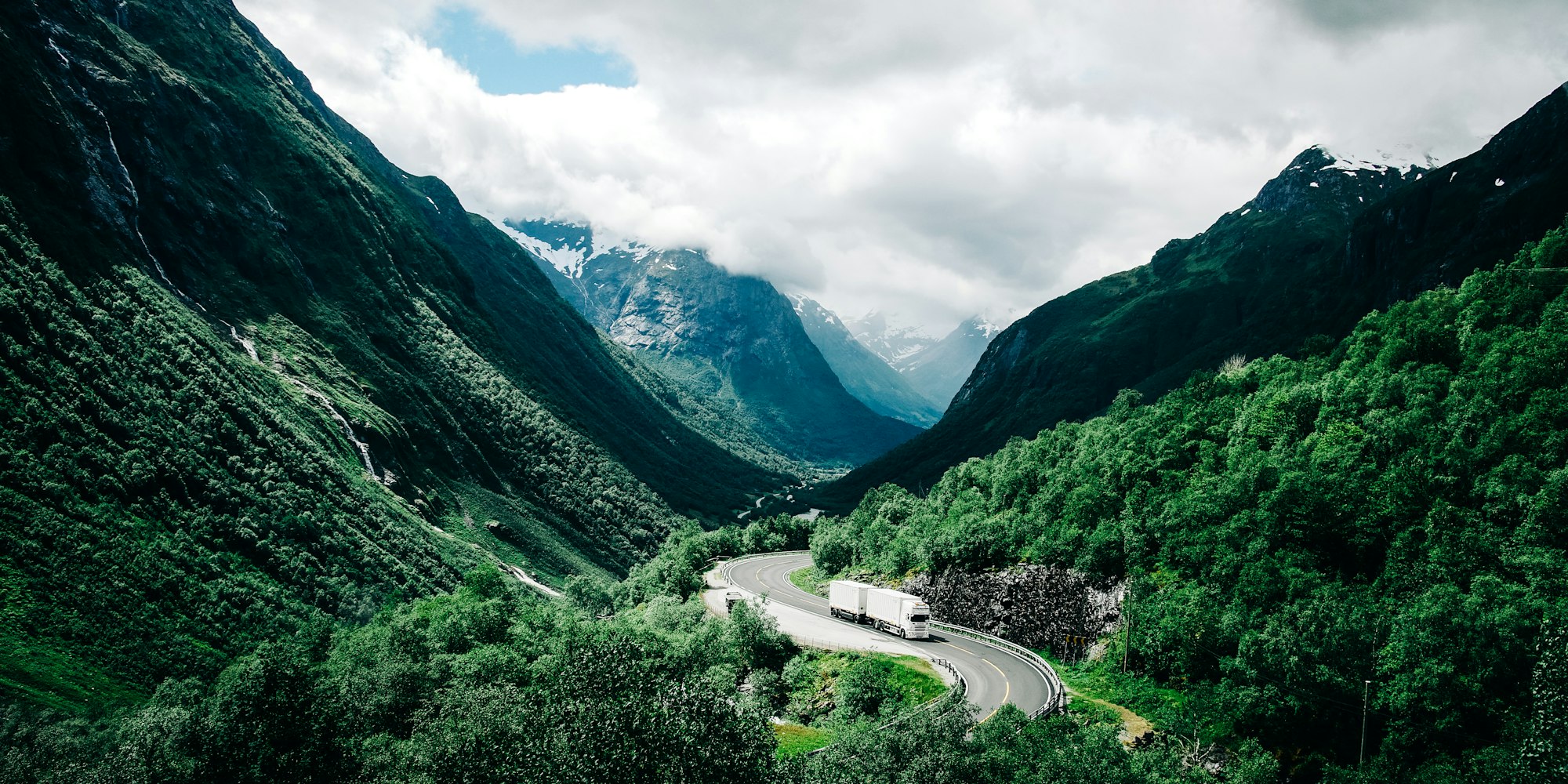 An articulated lorry on a winding road through a green Alpine valley