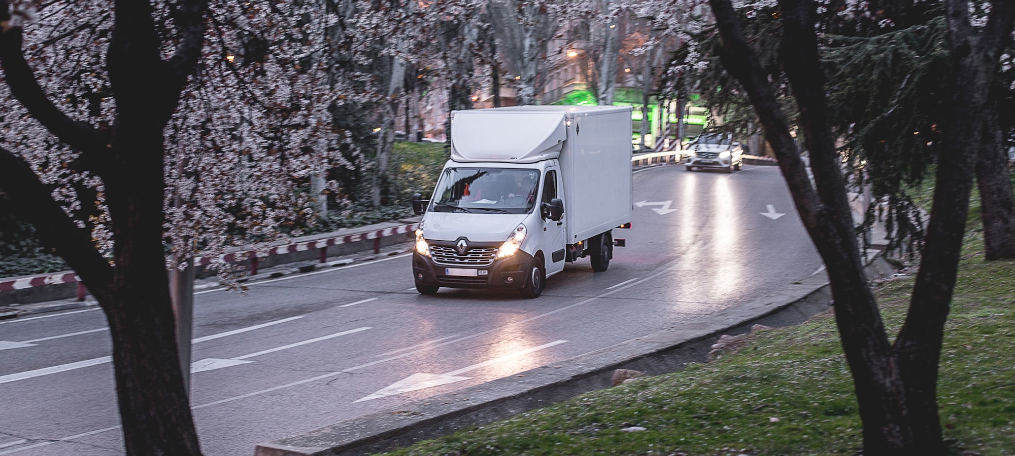 A white 3.5-tonne box van driving on a tree-lined road at dusk