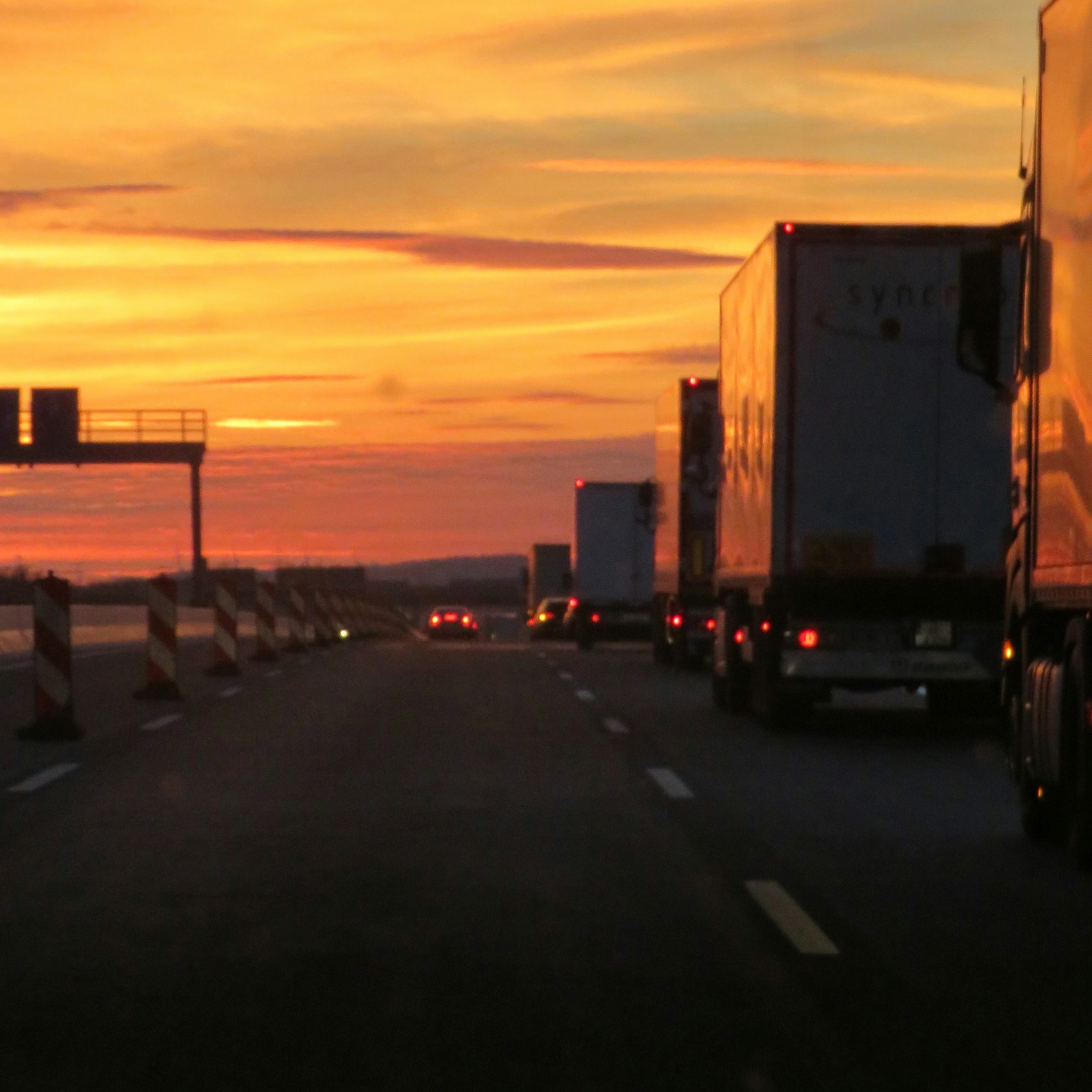 Lorries and cars on a German autobahn at sunset, roadworks markers along the hard shoulder