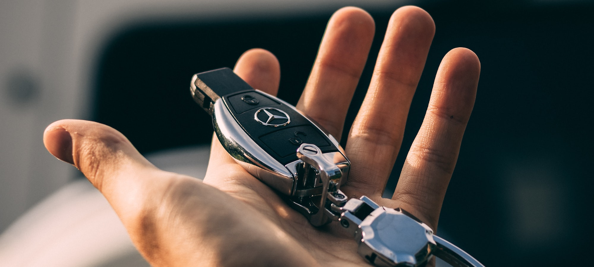 An open palm holding a car key in front of a vehicle